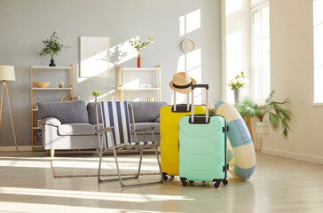 Colourful suitcases, chaise lounge, and rubber ring stand in an empty room at home, symbolizing...