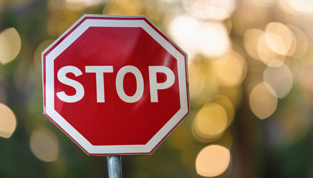 Classic red stop sign, octagon with bold white lettering, set against blurred bokeh background.
