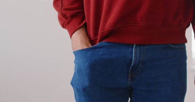 Unrecognizable man showing empty pockets of jeans, demonstrating bankruptcy and financial crises, being without money, spent all his savings, can not afford anything poses indoor