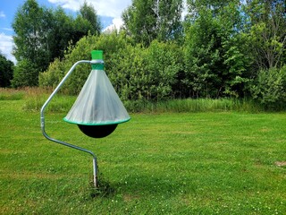 Horsefly trap against green trees. Photo of black ball insect trap on stand in mown meadow. Agricultural equipment for insect protection.
