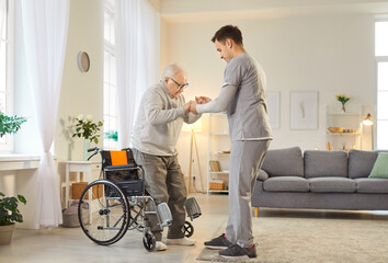 Portrait of a young male nurse helping a senior patient with disability to get off the wheelchair...