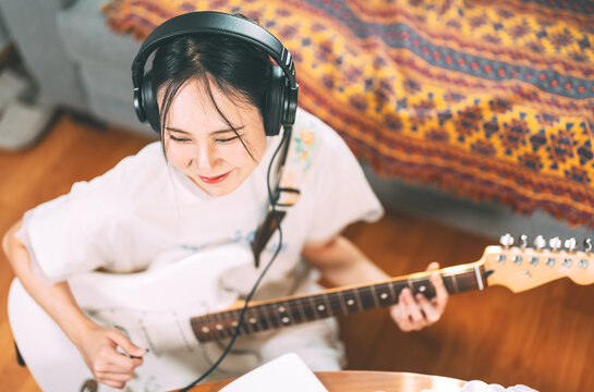 Young asian woman composer playing electric guitar wearing headphones