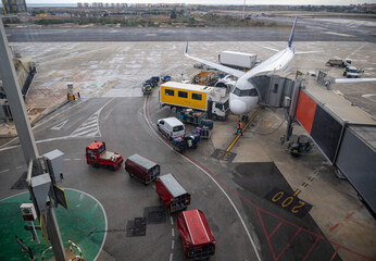Airport ground crew loading luggage into an aircraft's cargo hold under cloudy skies, showcasing vehicles, equipment, and runway activities at the terminal.