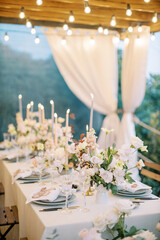 Set festive table with lit candles on a terrace with glowing garlands
