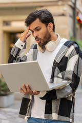 Displeased Indian man using laptop typing browsing working, loses becoming surprised sudden lottery...