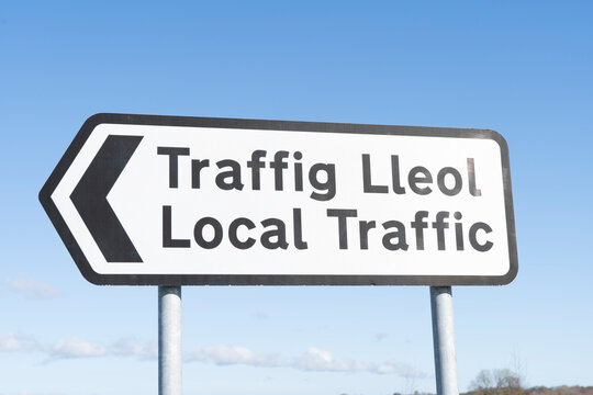 Sign for local traffic in English and Welsh against a blue sky.