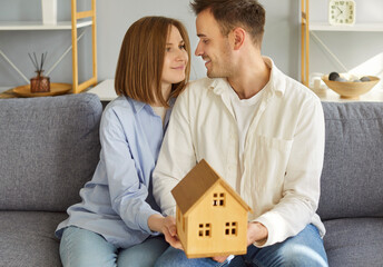 Loving family holding in hands small wooden tiny toy house, married couple after buying house,...