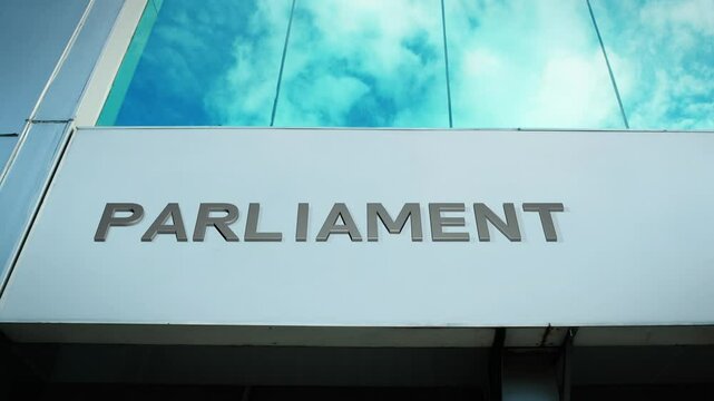 Parliament sign on a government building with a reflection of the sky on glass windows, symbolizing governance, lawmaking, and public service