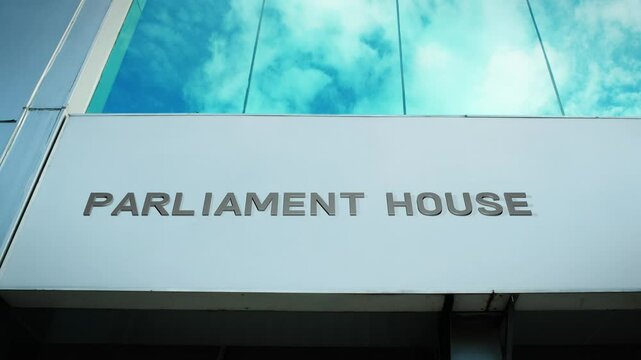 Parliament house sign on a government building with a reflection of the sky on glass windows, symbolizing governance, democracy, and public service