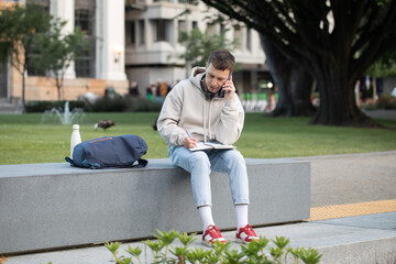 Obraz premium Young male freelancer conducts a work meeting on the phone in a public park. Businessman. 