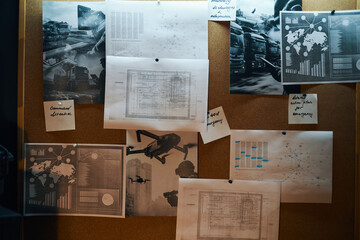 Diagram-covered papers pinned on corkboard, depicting various charts, graphs, and maps related to...