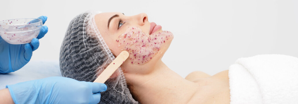 Close-up of a cosmetologist&rsquo;s hands applying an alginate mask with rose petals to a young woman&rsquo;s face in a professional beauty salon. Concept of skincare and relaxation in spa treatments.