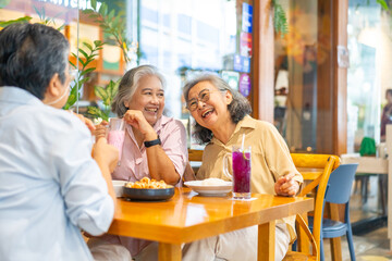 Fototapeta premium Happy Asian senior woman travel and shopping in the city on summer holiday vacation. Group of Healthy elderly women friends enjoy outdoor lifestyle having lunch eating food together at restaurant.