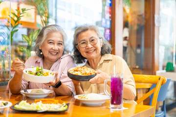 Happy Asian senior woman using mobile phone travel and shopping in the city on summer holiday vacation. Elderly women friends using smartphone taking selfie during having lunch together at restaurant.