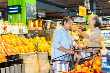 Happy Asian senior woman grocery shopping buying safety food at supermarket. Elderly women friends enjoy healthy lifestyle choosing and buying organic fresh food, vegetable and fruit at shopping mall.