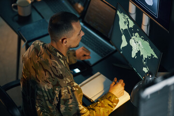 Military personnel in camouflage uniform analyzing global map on multiple high-tech computer...