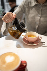 Female hand pouring natural herbal tea from teapot into cup on table
