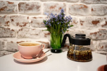 Herbal tea with in glass teapot  and cup on white table with flowers 