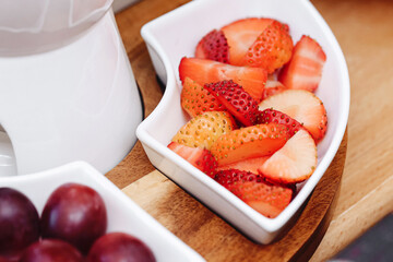Fruit fondue background. Sliced fruits for dipping in melted chocolate. Fresh strawberries and grapes prepared as a sweet and delicious dessert. Tasty and healthy snack for a fruit fondue experience.
