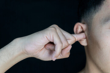 Man inserting his finger into his ear, possibly to relieve itching or discomfort. Dark background...