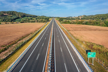 A vast, empty highway stretches across the Czech landscape, seen from above. Highway D6 from Prague to Karlovy Vary and Cheb.