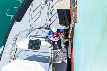 Aerial, top view on the pilot boat - pilot preparing to enter cargo ship using gangway, he will...