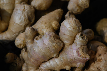 Fresh organic ginger roots piled together in a dimly lit market stall ready for culinary use