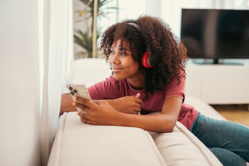 Happy African woman relaxing on the sofa at home. Smiling girl enjoying holiday sitting on couch,...