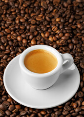 Small white espresso cup with saucer, nestled among bed of roasted coffee beans, creating cozy and inviting atmosphere perfect for enthusiasts