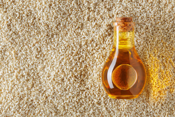 Glass bottle containing golden oil is placed on sesame seeds creating visually appealing contrast...
