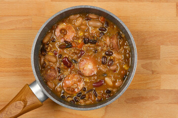 A top-down shot of a pot of bean stew with sausage slices, showcasing a hearty and rustic meal on a wooden surface