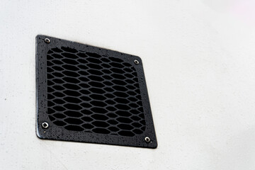 A black metal grate or vent cover with an oval pattern, mounted on a light-colored, possibly white, surface.