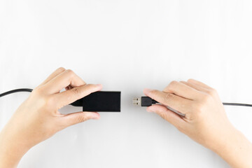 A pair of hands are shown connecting a black USB cable to a power adapter against a white surface backdrop