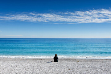 Solitary figure sitting on a serene beach gazing at the calm ocean