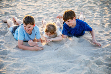 Three children playing with sand on sunset ocean beach. happy family, two school boys and one little preschool girl. Siblings having fun together. Bonding and family vacation in Andalucia, Spain