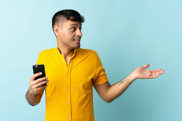 Young Colombian man using mobile phone isolated om blue background with surprise facial expression