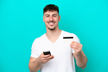 Young caucasian handsome man isolated on blue background buying with the mobile with a credit card
