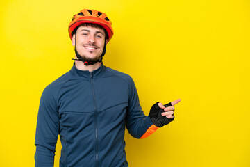 Young cyclist caucasian man isolated on yellow background pointing finger to the side