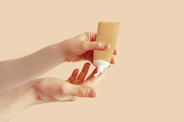 Squeezing cream from a tube onto a finger. A tube of cream in the hands of a Caucasian woman. Beige mocha background.