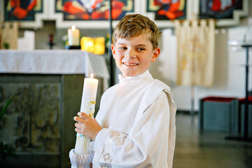 Little kid boy receiving his first holy communion. Happy child holding Christening candle....