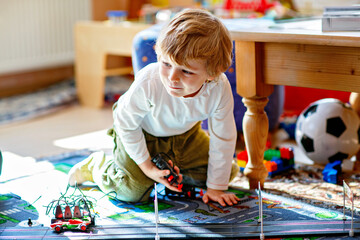 Happy cute preschool boy playing with racing cars on racetrack, indoors, with cars. Excited child...