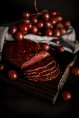 meat balyk on a wooden board with purple large grapes on a black background