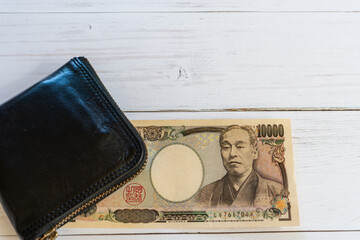 旧一万円札と黒い財布、白い木目調テーブル