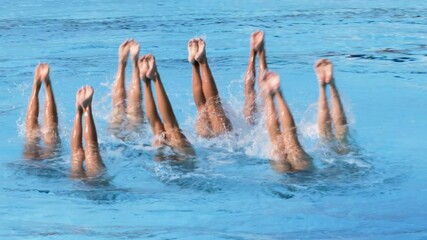 Synchronized or artistic swimmers performing an elegant and precise water routine with their legs gracefully in swimming pool