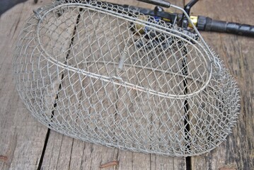 metal mesh for caught fish on a wooden table and a blurred fishing rod in the background. selective focus