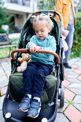 Little girl sits in the yard in a stroller, holding the handle