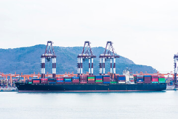 Busan, South Korea - large cargo ship, berthed under gantry cranes in the container terminal. She is fully loaded with colorful containers.