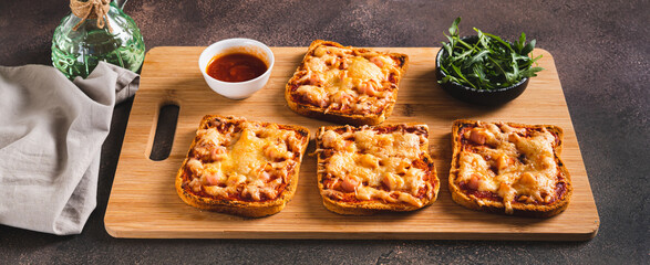 Baked sandwiches with bacon, cheese and tomato sauce on a board on a table web banner
