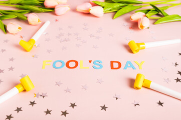 April Fools' Day written in colored letters, whistles, stars and tulips on pink