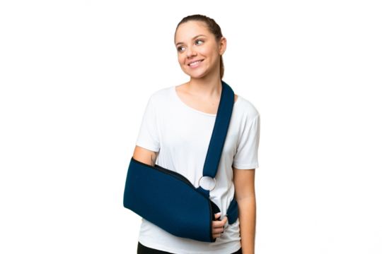 Young blonde woman with broken arm and wearing a sling over isolated chroma key background looking to the side and smiling